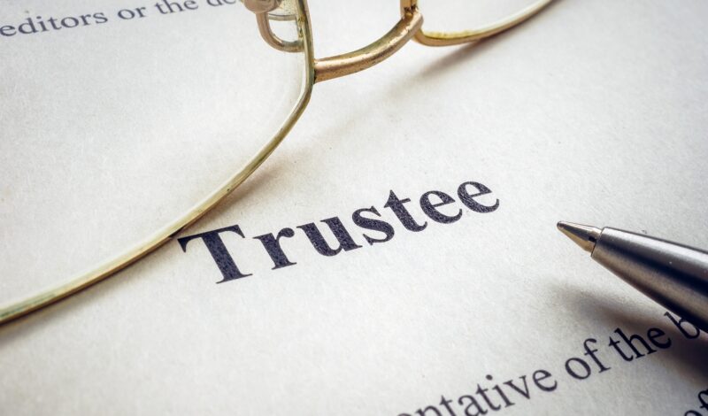 Word trustee near glasses and a pen.